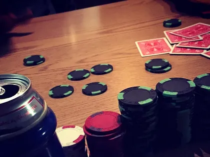 Poker chips and playing cards spread across a wooden table beside an open can of beer, mid-game