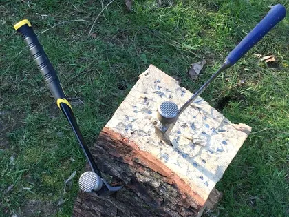 Two well-used mallets resting on a split log outdoors, the block beneath them chewed up from years of use