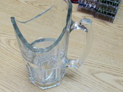 A glass pitcher engraved POKER CHAMPION with its top smashed clean off, on a table beside racks of poker chips