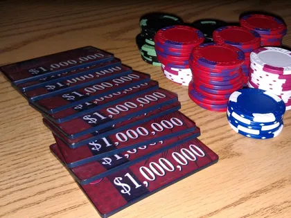 A fanned stack of one-million-dollar poker plaques beside stacks of red, white and blue chips on a wooden table